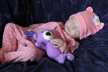 A baby doll resting on a soft purple blanket, showcasing its delicate features and bright clothing.